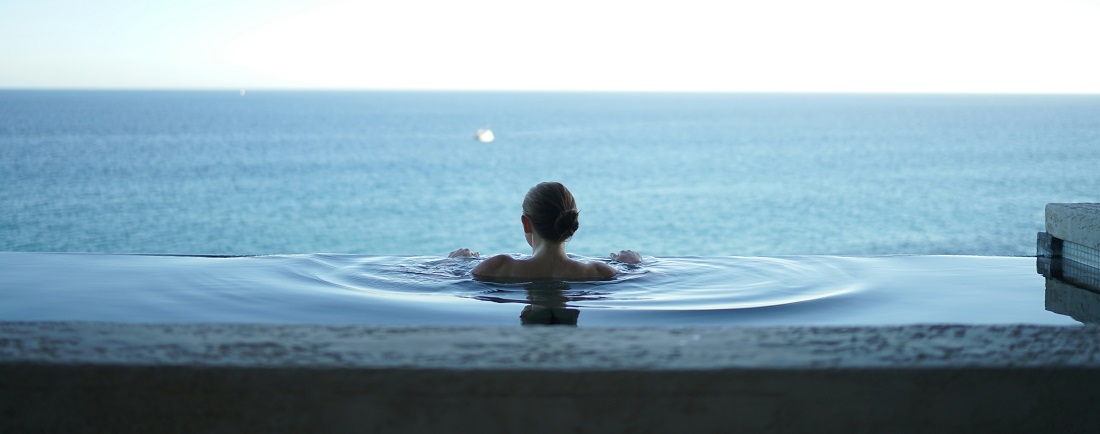 Woman in a pool overlooking the ocean by Alex Bertha