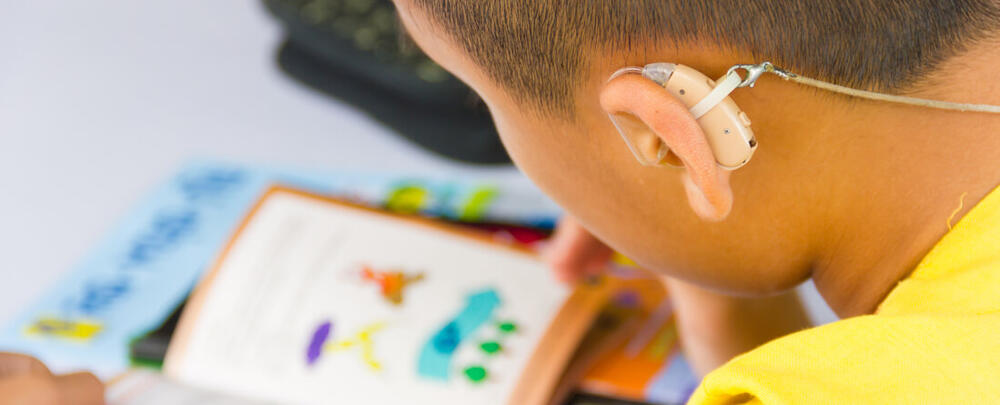 learner with hearing aid reading a school book