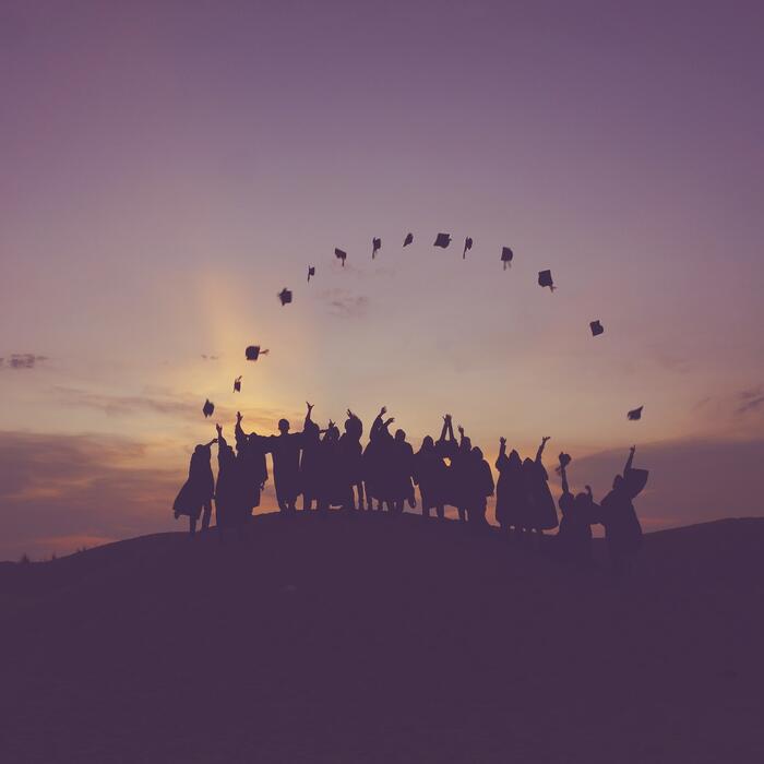 silhouettes of graduates throwing their caps during sunset